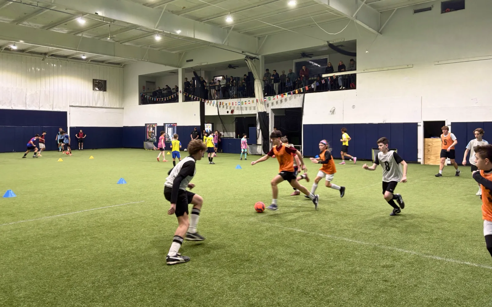 Kids in pinnies racing for the ball during an indoor turf party game.